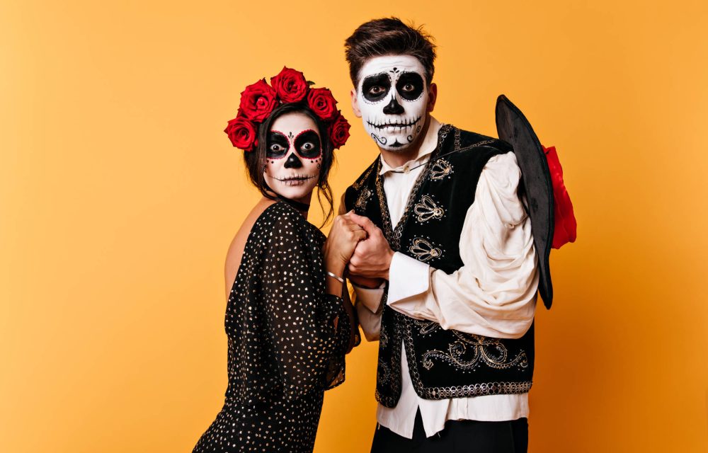 Portrait of pair of lovers on isolated orange background. Girl and guy in form of skeletons hold hands in fright